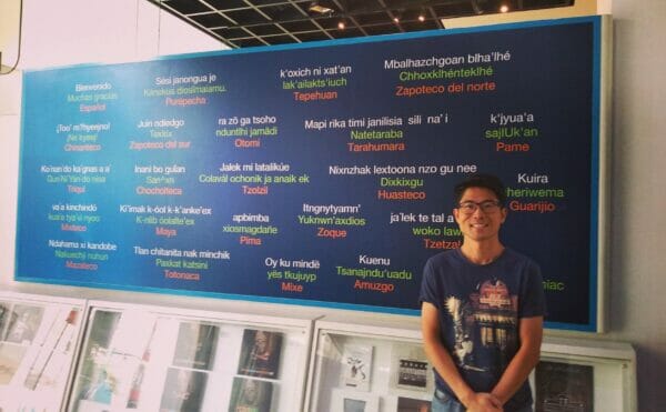 Isao Iwasaki, a Mexican tourist guide, is giving greetings in front of a board with various languages ​​written on it.