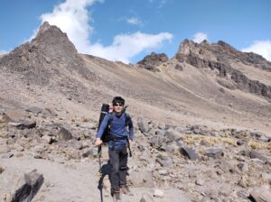 高山で山をバックにポーズをとるメキシコガイドの岩﨑功