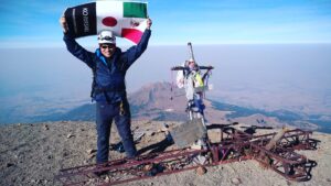 Isao Iwasaki, a Mexican guide holding the national flags of Mexico and Japan against the blue sky at the top of a mountain