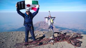 山の頂上で青空をバックにメキシコと日本の国旗を掲げているメキシコガイドの岩﨑功