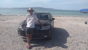 Mexican tourist guide Isao Iwasaki poses in front of a car with the sea in the background