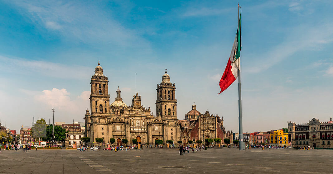 メキシコシティのソカロで風にたなびく国旗と日を浴びる大聖堂カテドラル