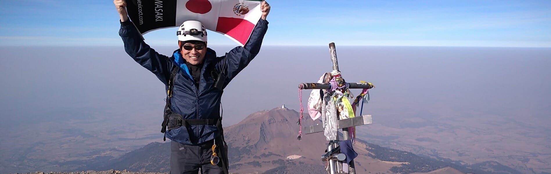 A person holding the Mexican and Japanese flags on a mountaintop