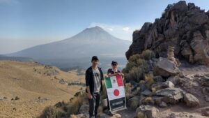 高山をバックに男女二人が日本とメキシコの国旗を掲げている
