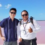 サングラスを掛けた二人の男性がピンク色の湖をバックにポーズをとっている